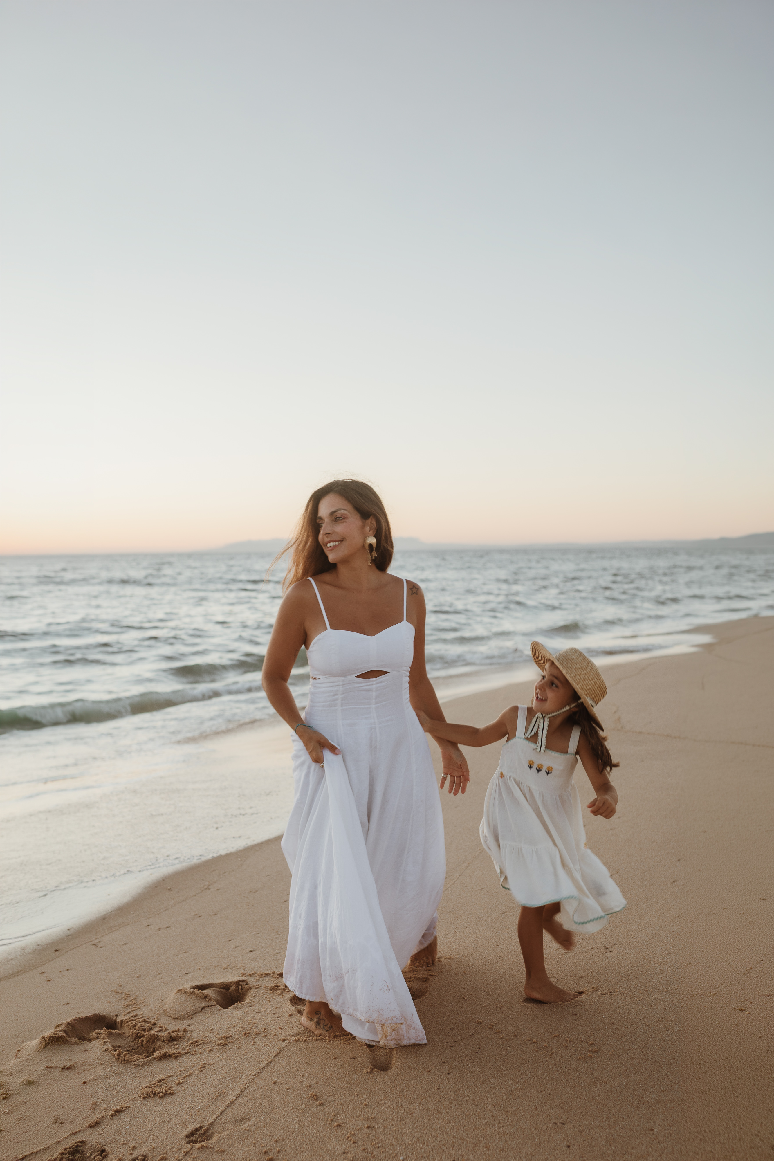 Mãe e filha a correr na praia, vestidas de branco