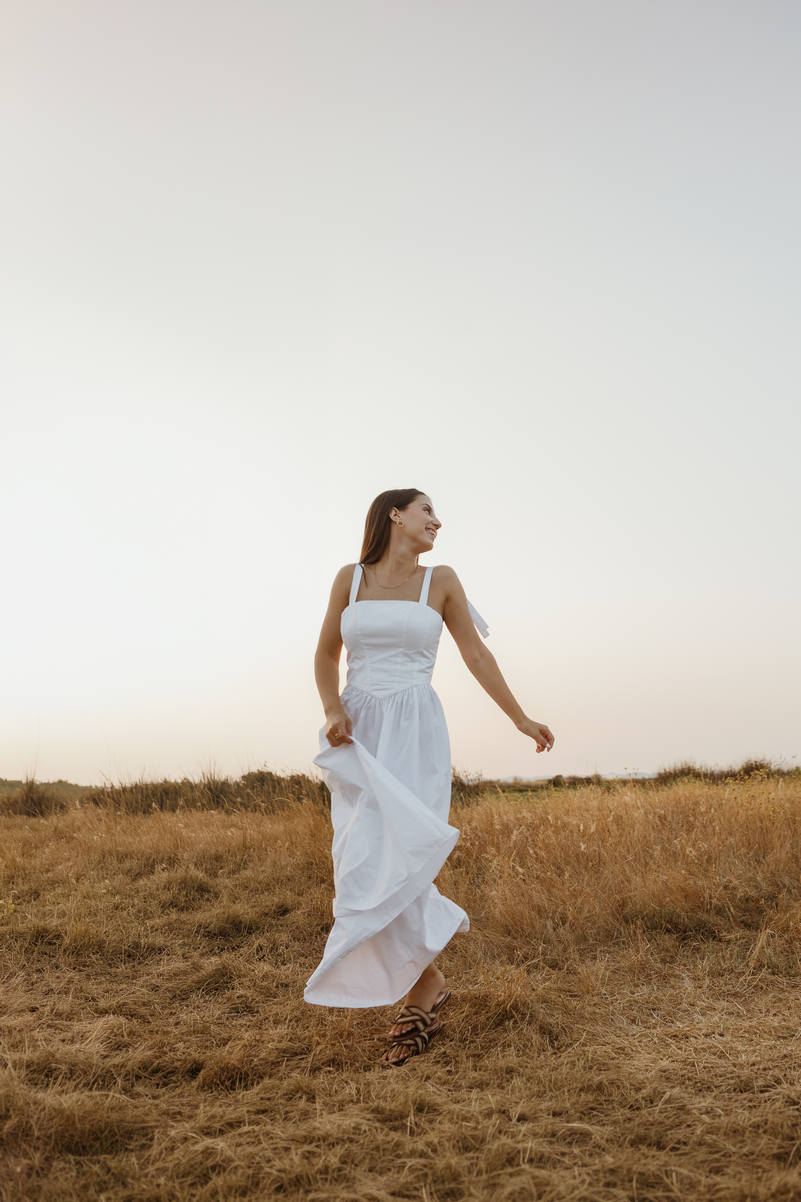 Mãe de vestido branco a rodopiar, no campo ao pôr do sol