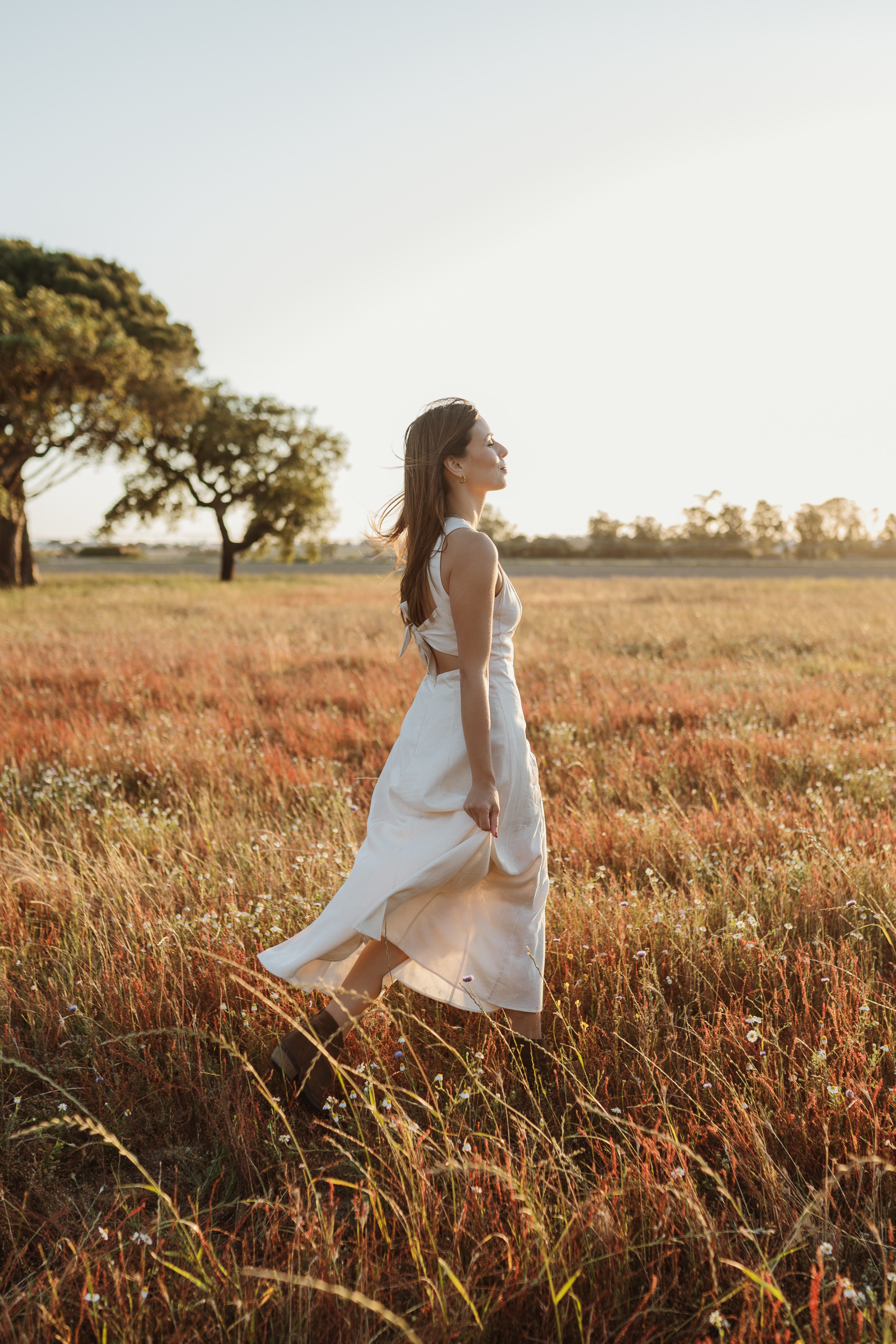 Mulher de vestido branco a caminhar num campo dourado ao pôr do sol