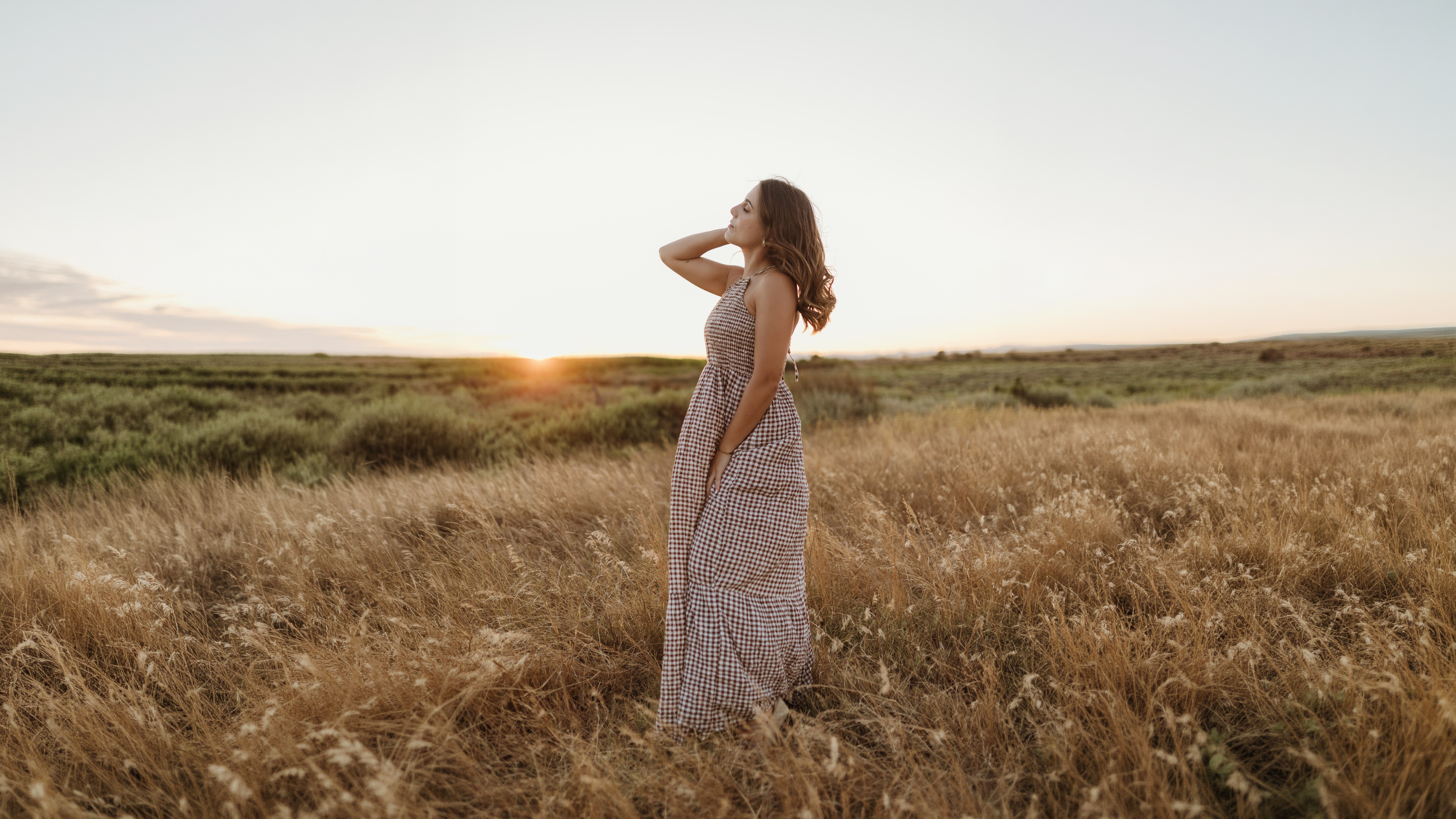 Mulher de vestido às quadrados num campo dourado, ao pôr do sol
